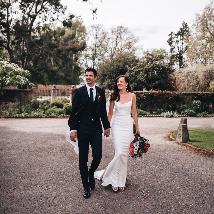 Luxe bride and groom in front of walled garden at their stately home wedding in the Cotswolds brides makeup by Jessica Rose