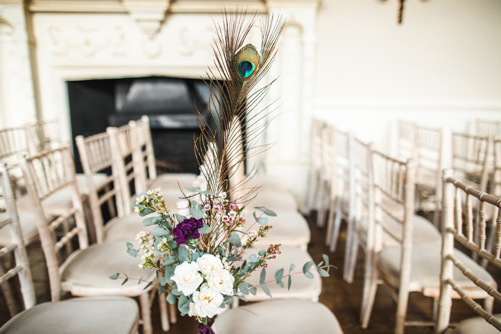 Peacock feathers and flowers decorate the chairs in the aisle of this epic weekend long wedding