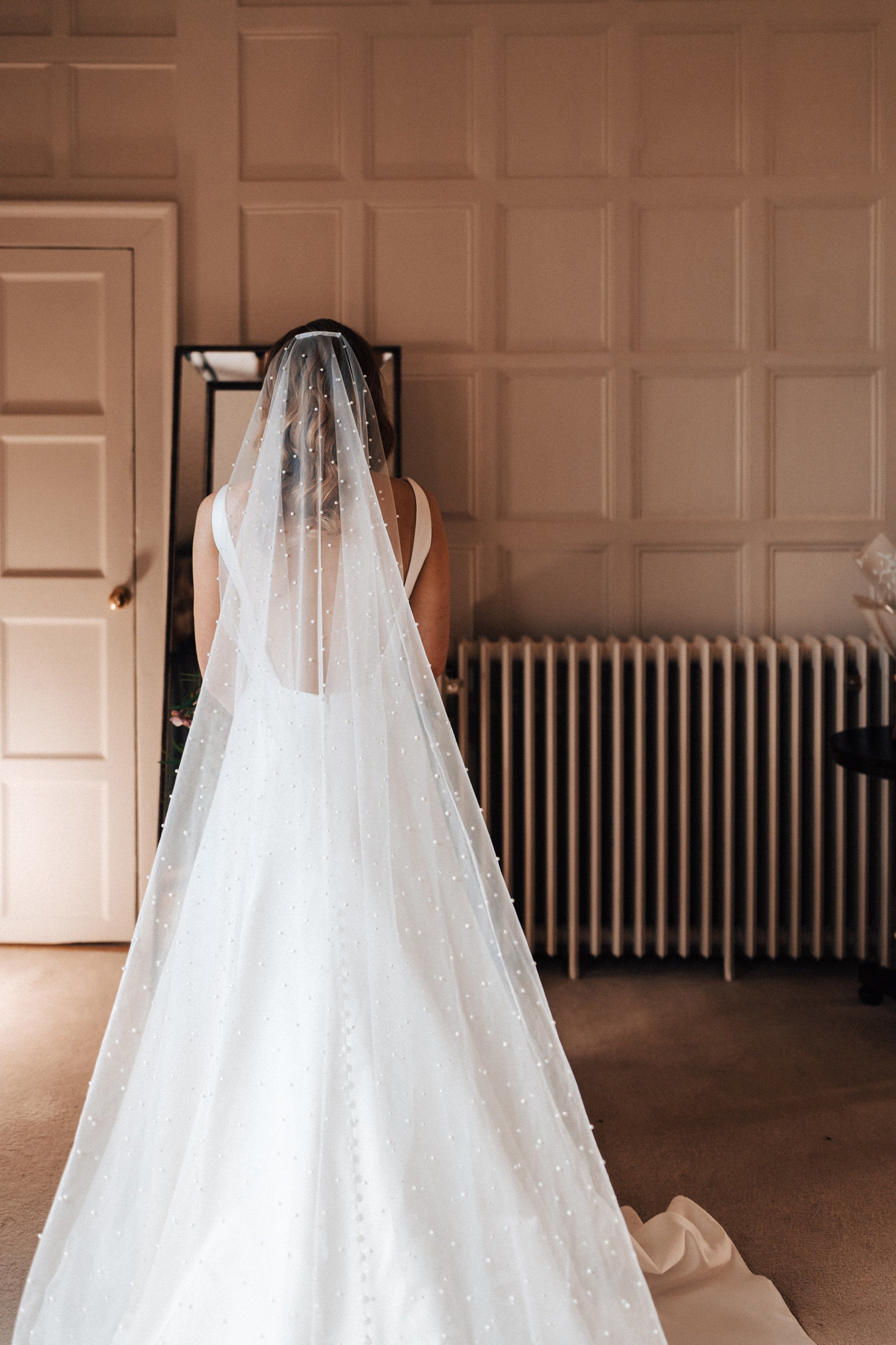 Cathedral length pearl veil on bride standing in stately home bridal suite at elmore court