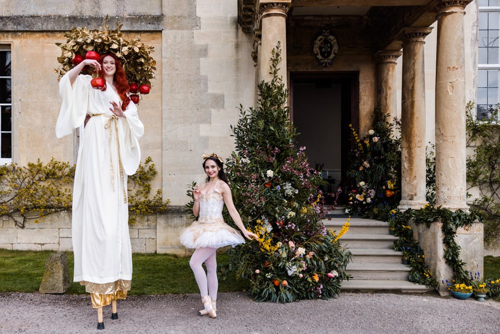 Unusual wedding venue open day beautiful stately home entrance decorated with flowers and festival wedding performers dressed in white on stilts greeting guests