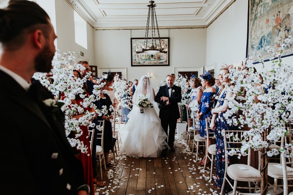 Veiled bride walks down aisle on her Easter wedding with white blossom trees