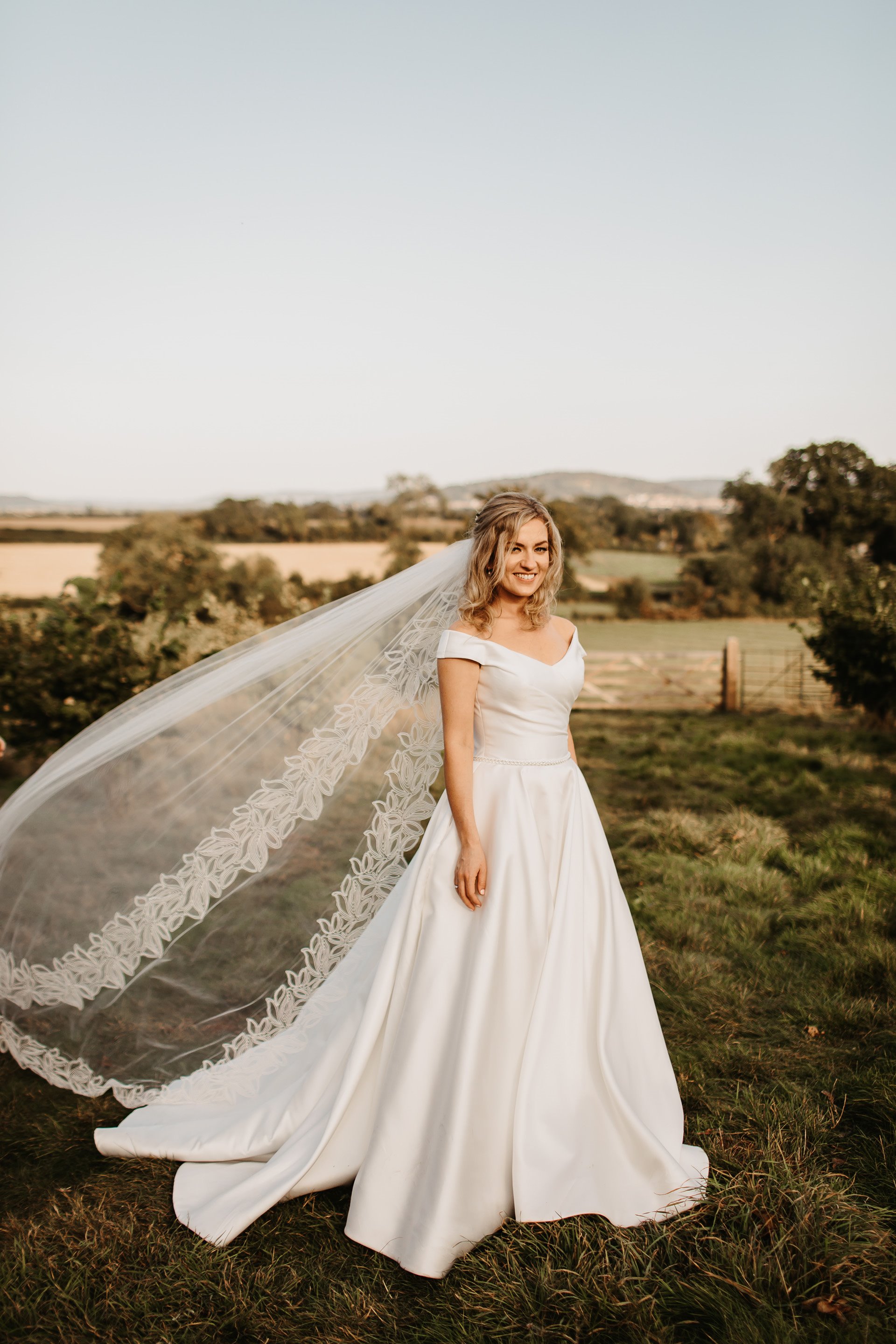Bride wearing a floor length veil outside in the countryside on her wedding day