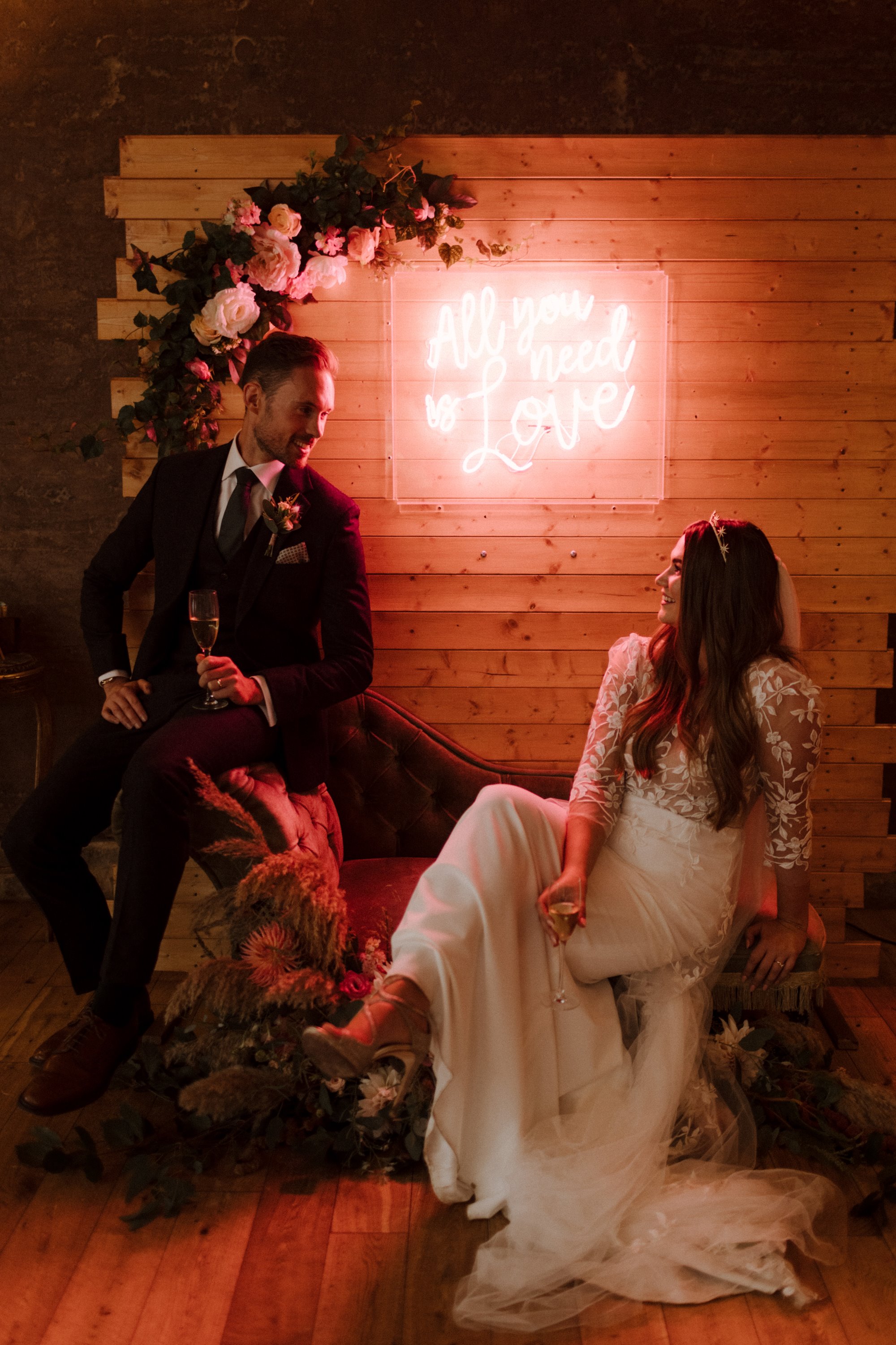 beautiful newly wed couple sitting in front of a neon sign while gazing into each others eyes