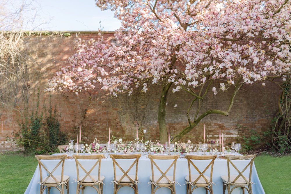 Rehearsal wedding dinner table set up underneath the magnolia tree in the walled garden at cotswolds wedding venue elmore court