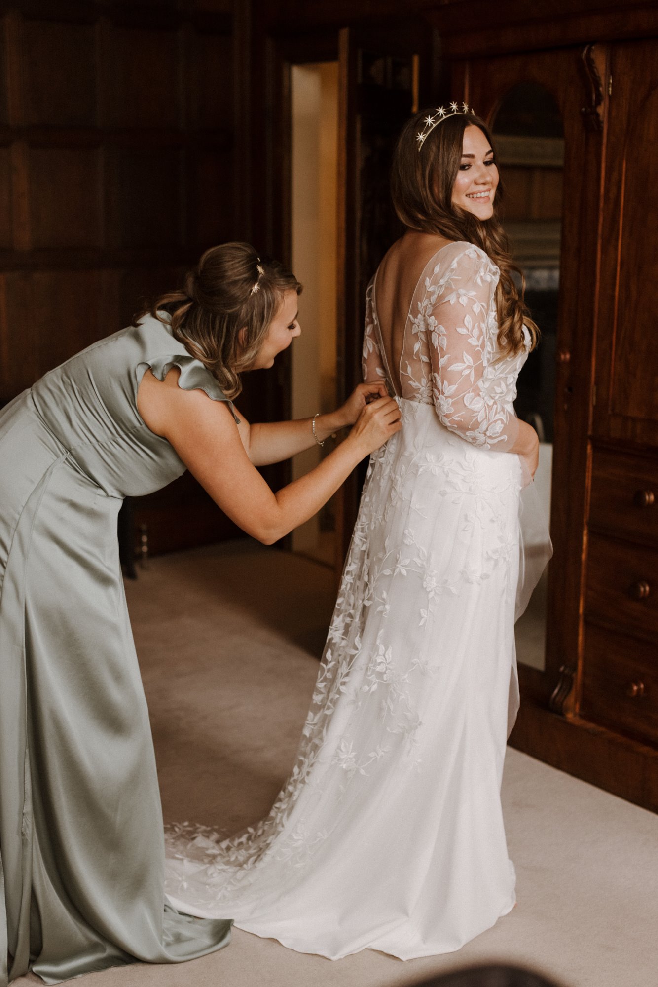 beautiful boho bride getting into her long french lace dress in stately home bedroom