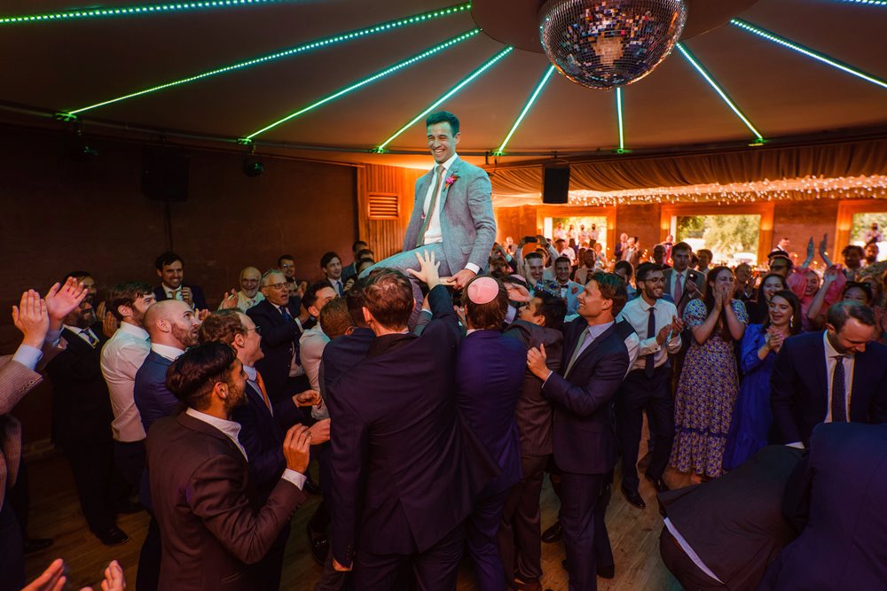 Groom held up above guests at raucous party at jewish wedding