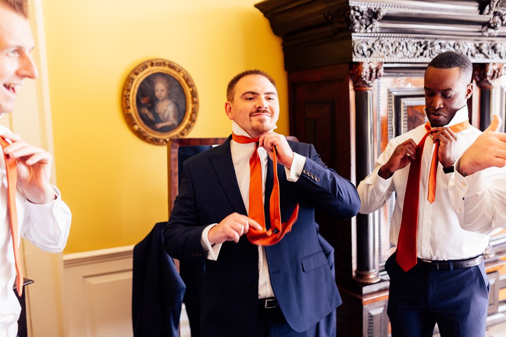 groomsmen get ready for wedding in colourful room in stately home