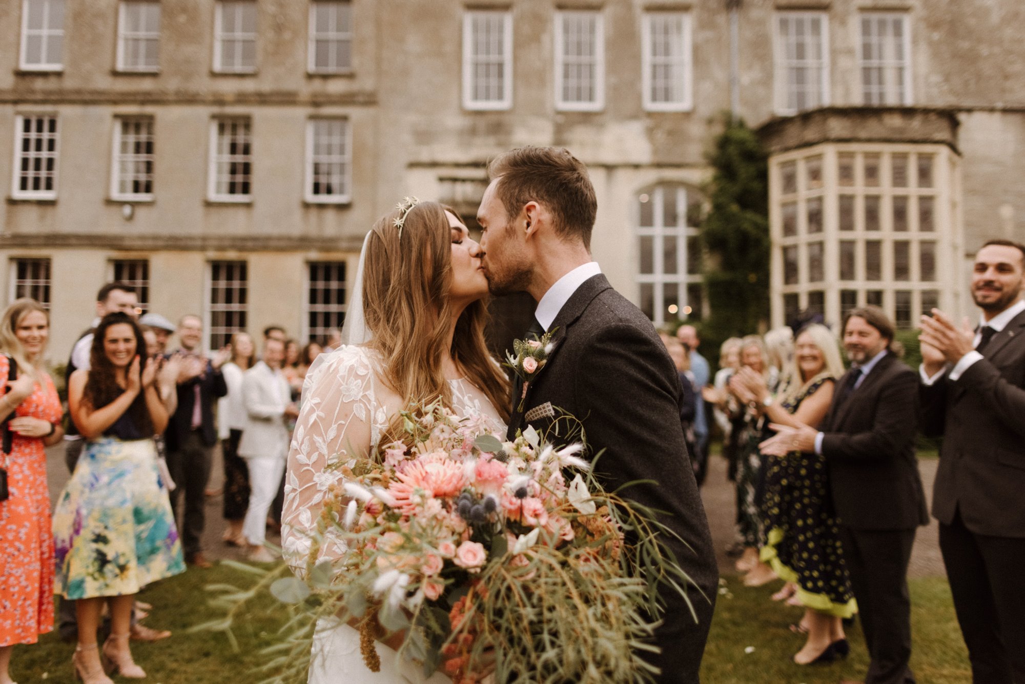 Modern boho luxe couple kiss outside stately home wedding venue elmore court bride wears star tiara and lace dress