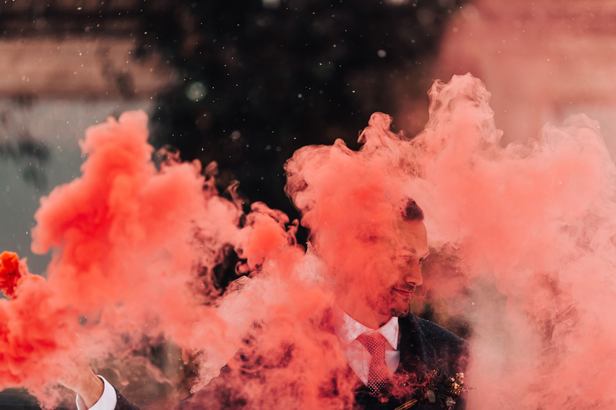 Coral coloured smoke from a smoke bomb obscures part of grooms face in a beautiful cloud of bright colour