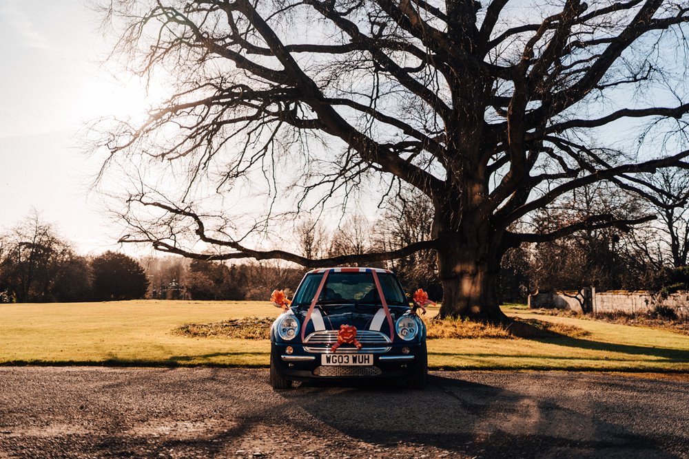 mini with red ribbons under beautiful tree decorated for a christmas wedding in the cotswolds