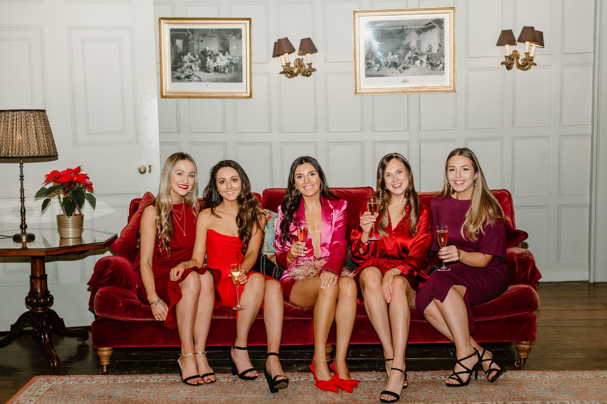 Bridal party all in beautiful red dresses sitting on a sofa in a stately gloucestershire home