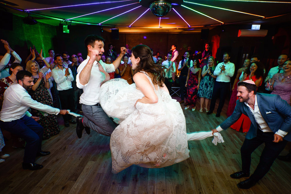 Jewsih wedding party newlywed couple skipping together in rope made of napkins with huge smiles on their faces at party wedding venue elmore court