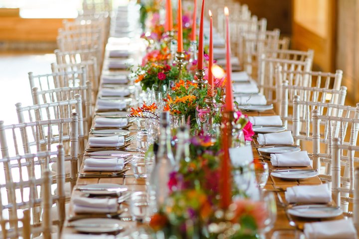 Pink and orange wedding theme reception with flowers and real candles on long wooden tables in The Gillyflower at Elmore Court for a Jewish summer wedding