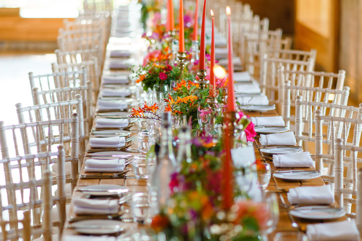 Pink and orange wedding theme reception with flowers and real candles on long wooden tables in The Gillyflower at Elmore Court for a Jewish summer wedding