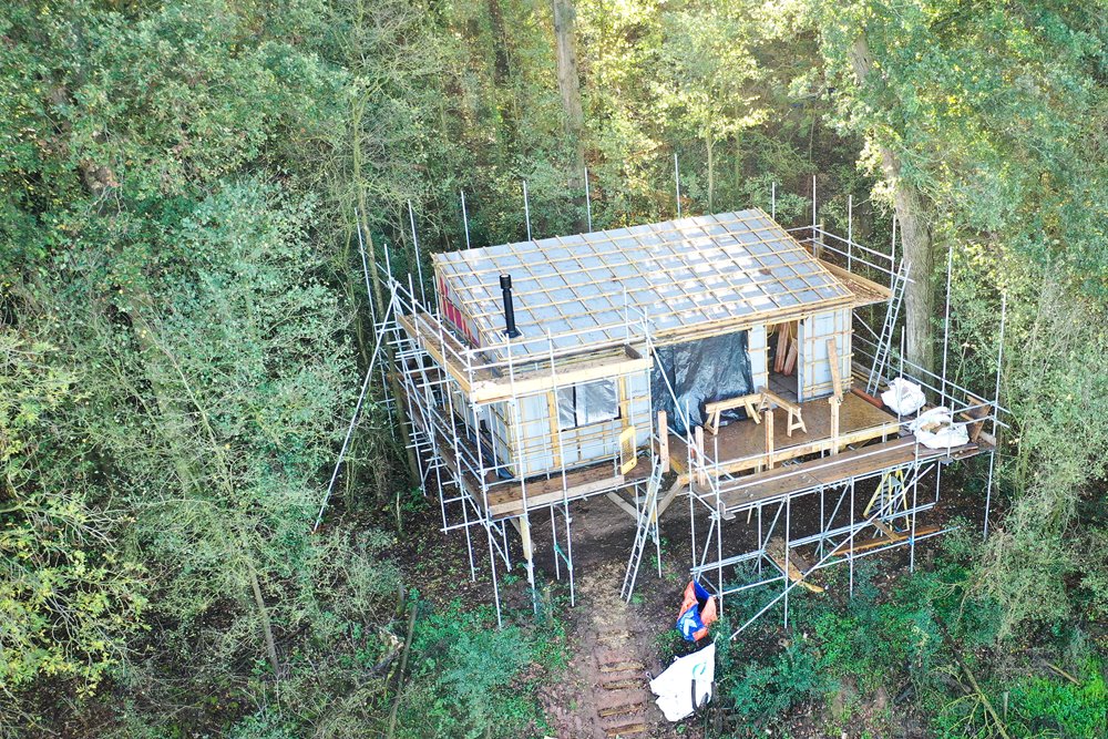 A small treehouse cabin being built in a beautiful English Woodland at Elmore Court, with sunlight shining through the trees
