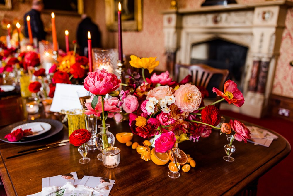 Colourful wedding inspiration of bright bold pink and red florals, citrus fruits and red candlesticks on table at wild wedding fair in gloucestershire 2022