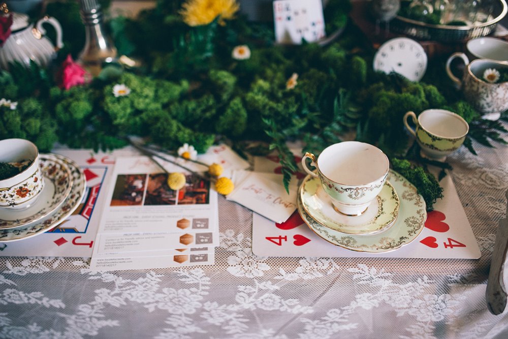 ALice in wonderland tea party set up on tables with cards and tea cups for a garden wedding with a festival twist