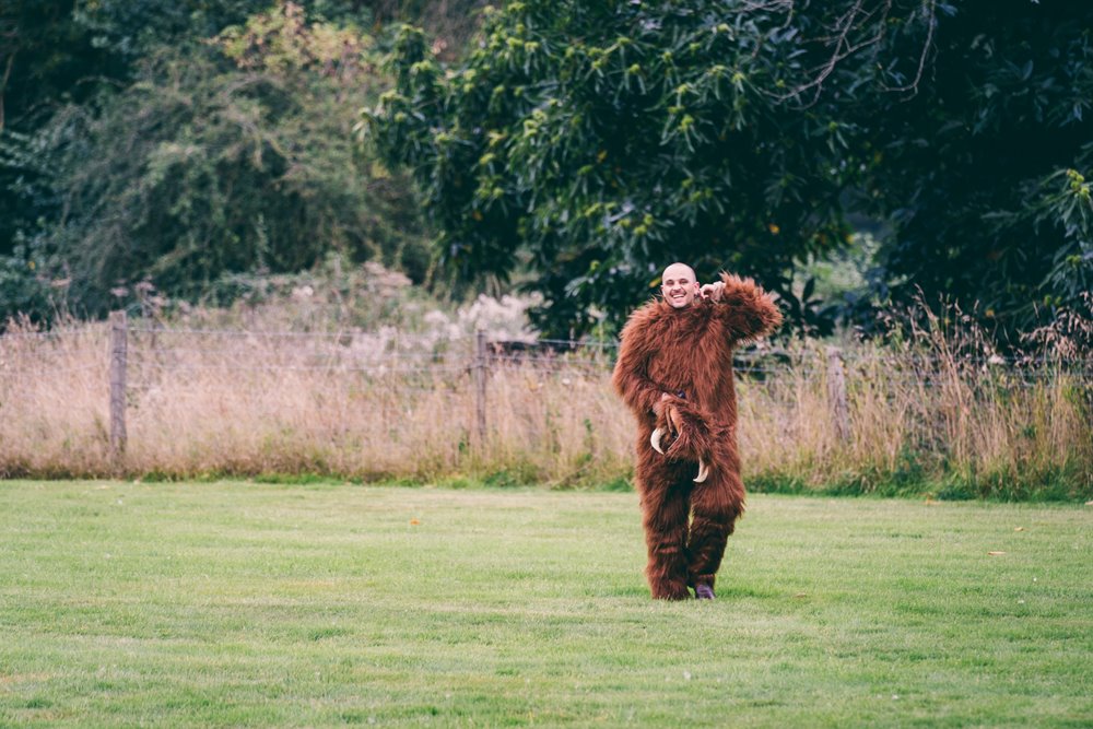 Man wearing bear suit walks through gillyflower meadow for a secret garden party inspired wedding