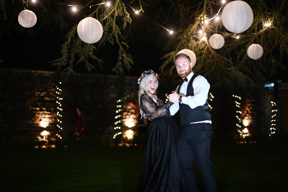 moody photoshoot with bride in black wedding dress and magical lanterns on trees