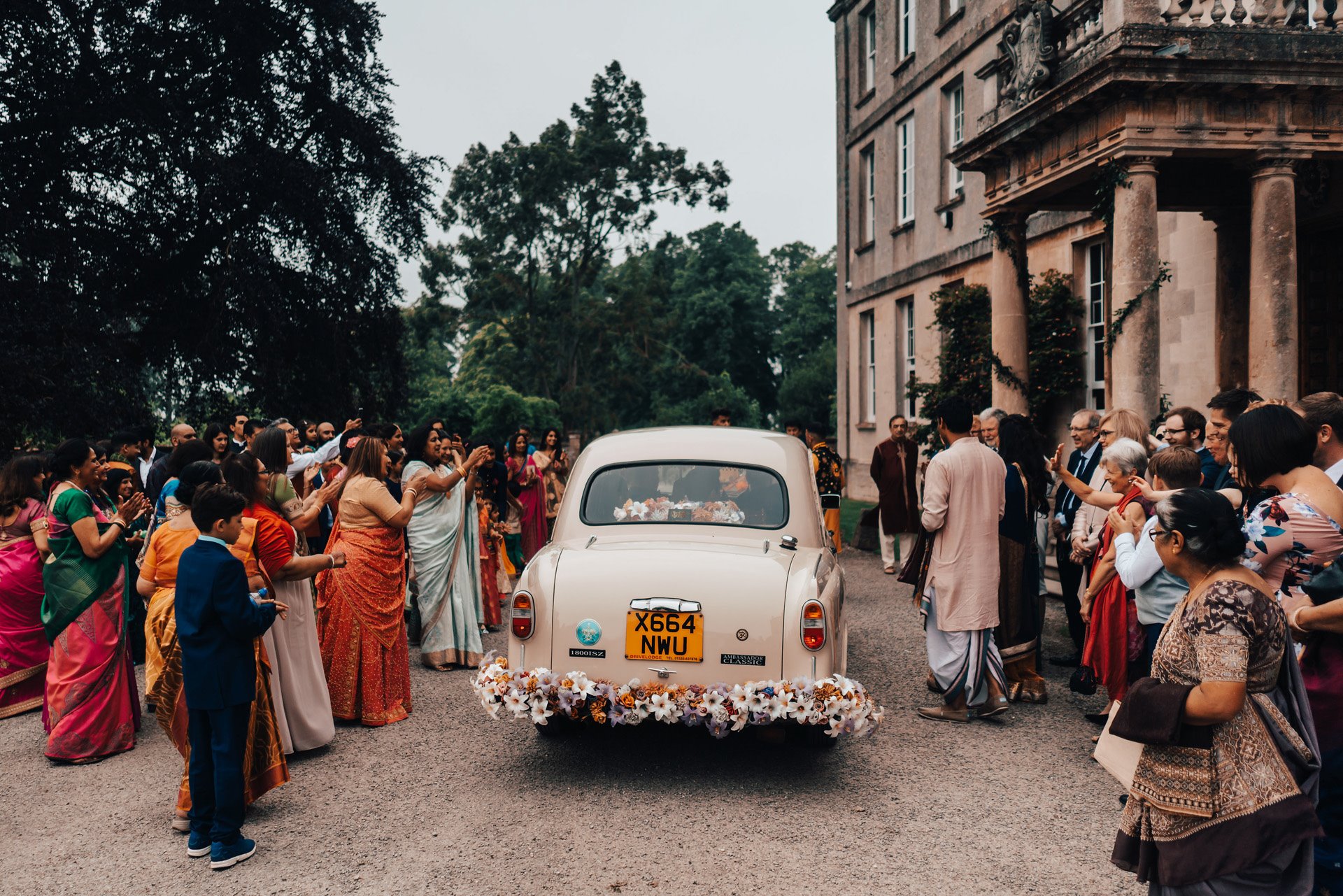 Indian wedding groom arrival baraat in beautiful old car decorated with flowers outside mansion house elmore court