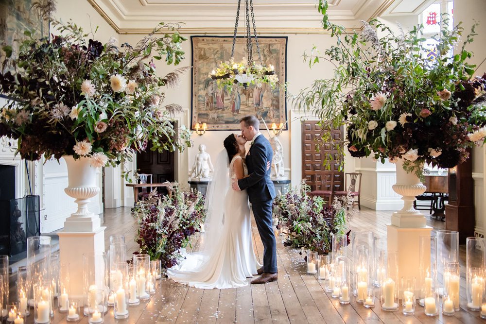 Micro wedding couple kiss in an aisle surrounded by candles, huge flowers in urns and foliage