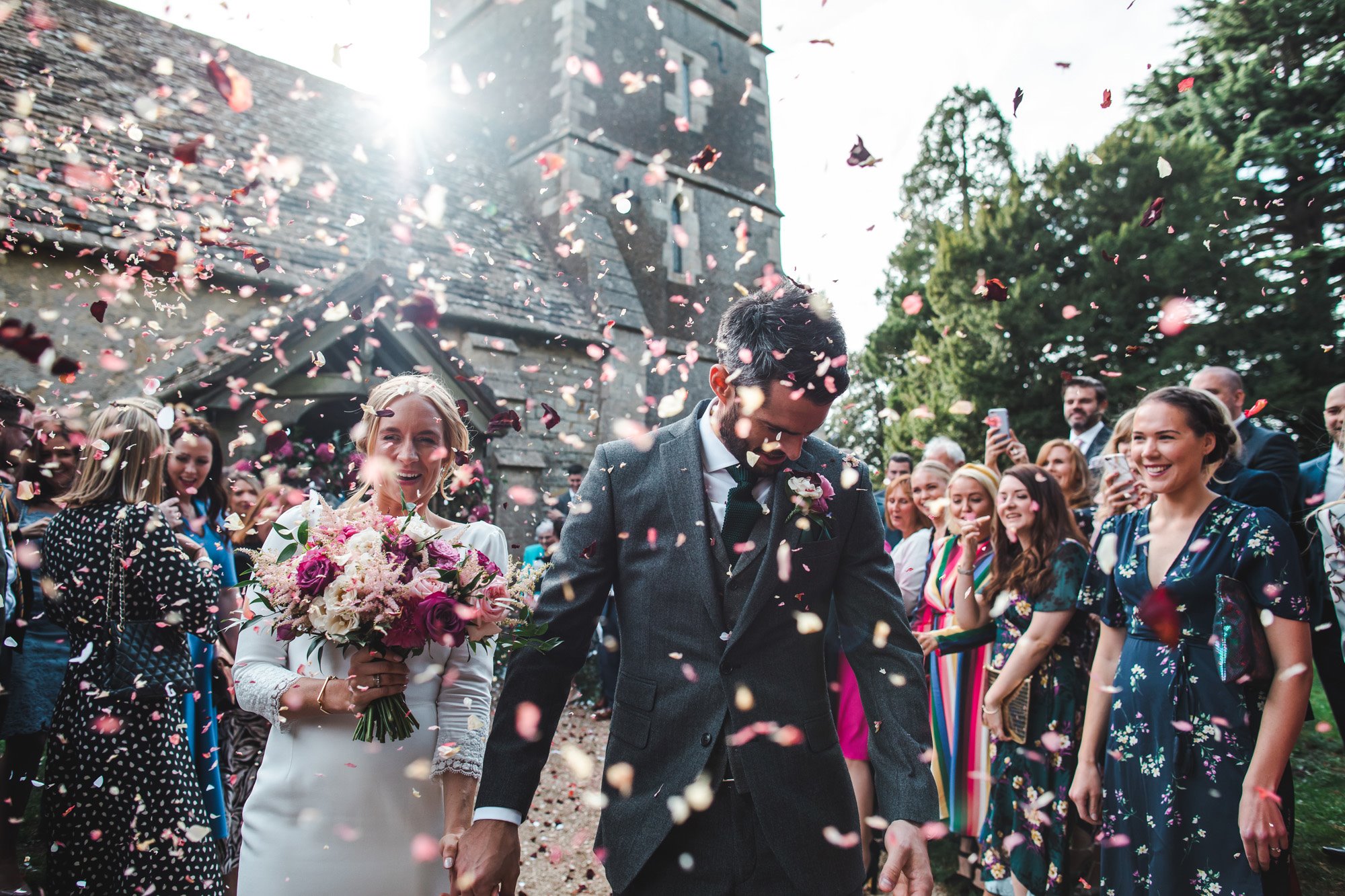 Explosion of rose petal confetti as happily newlywed couple leave Elmore church in Gloucestershire just after their marriage ceremony