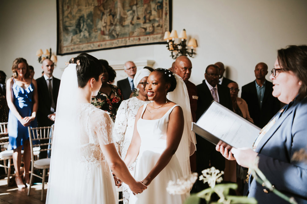 Magical lgbtq wedding ceremony with two brides holding hands saying vows in mansion house hall