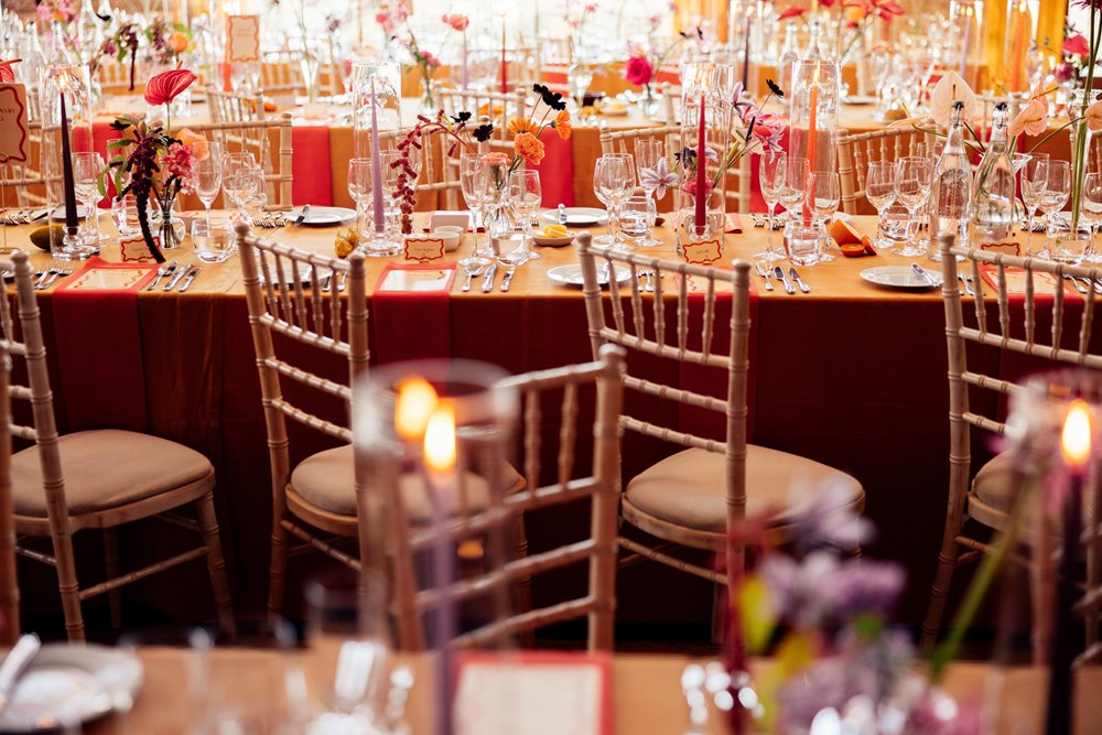 Colourful wedding reception. Orange tables with bright flowers at eco venue in the cotswolds