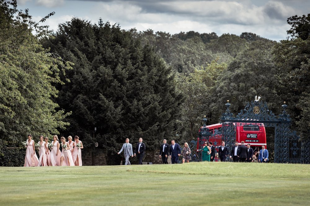 Summer wedding guests arrive by double decker red bus at elmore court