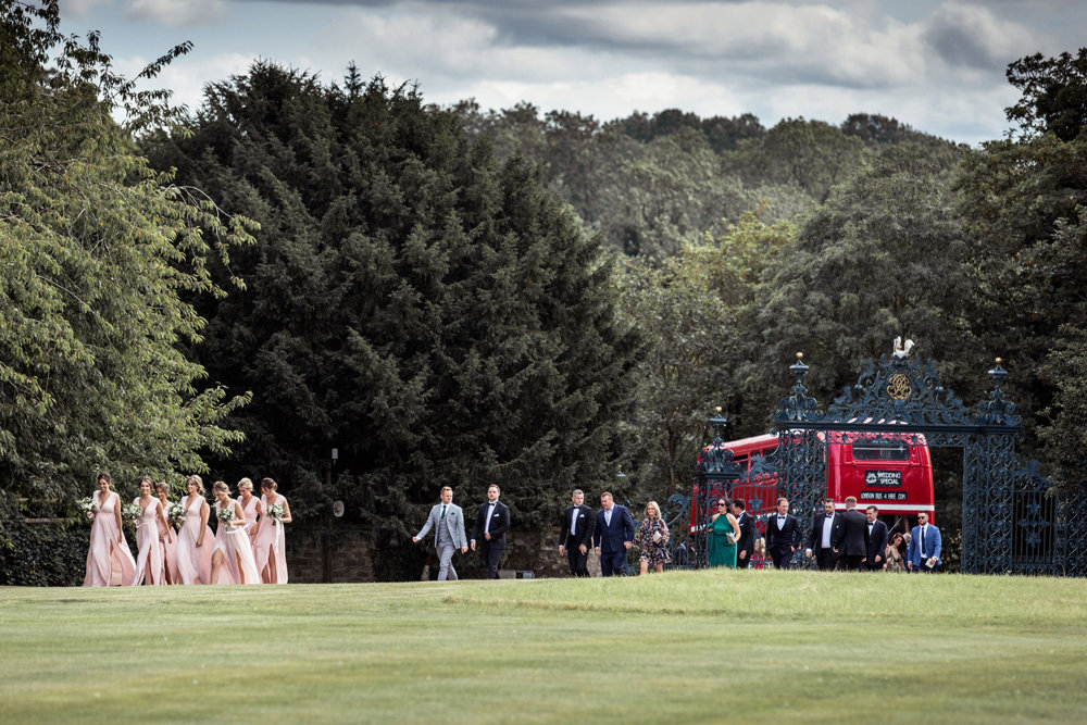 Summer wedding guests arrive by double decker red bus at elmore court