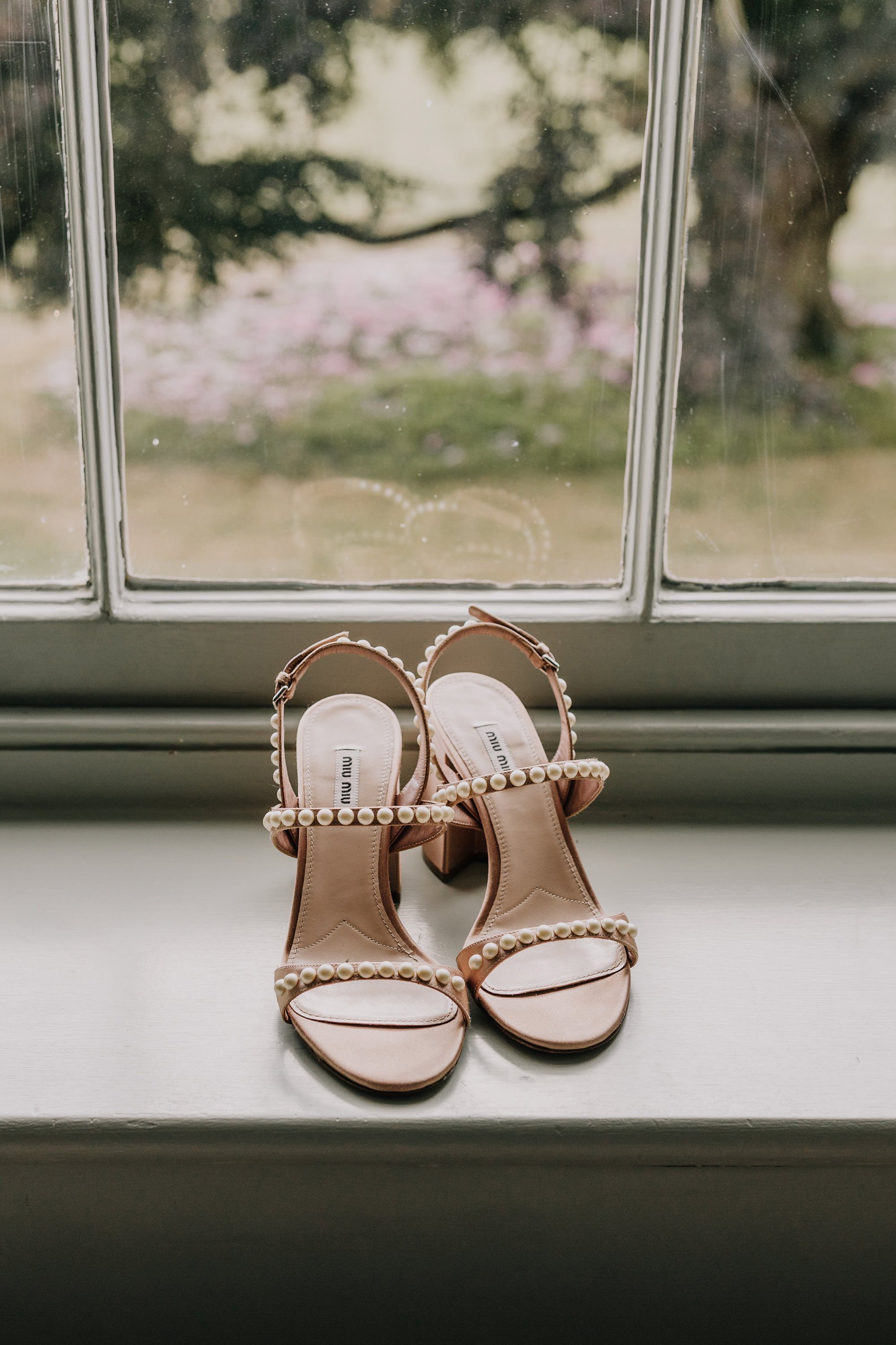 Delicate pearl wedding shoes with pearl straps by Miu Miu on windowsill of stately home wedding venue