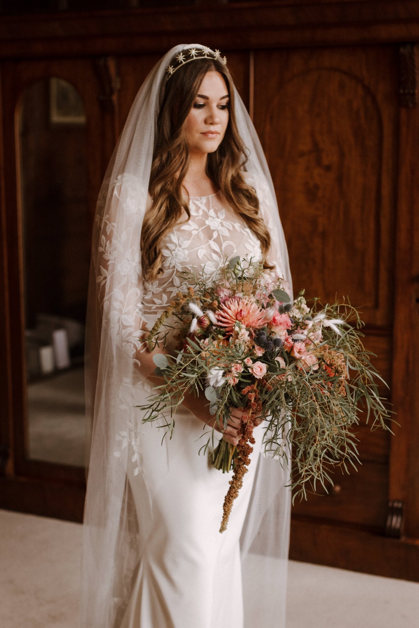 beautiful boho bride in lace gown, star crown, long veil and trailing bouquet of pink and greenery
