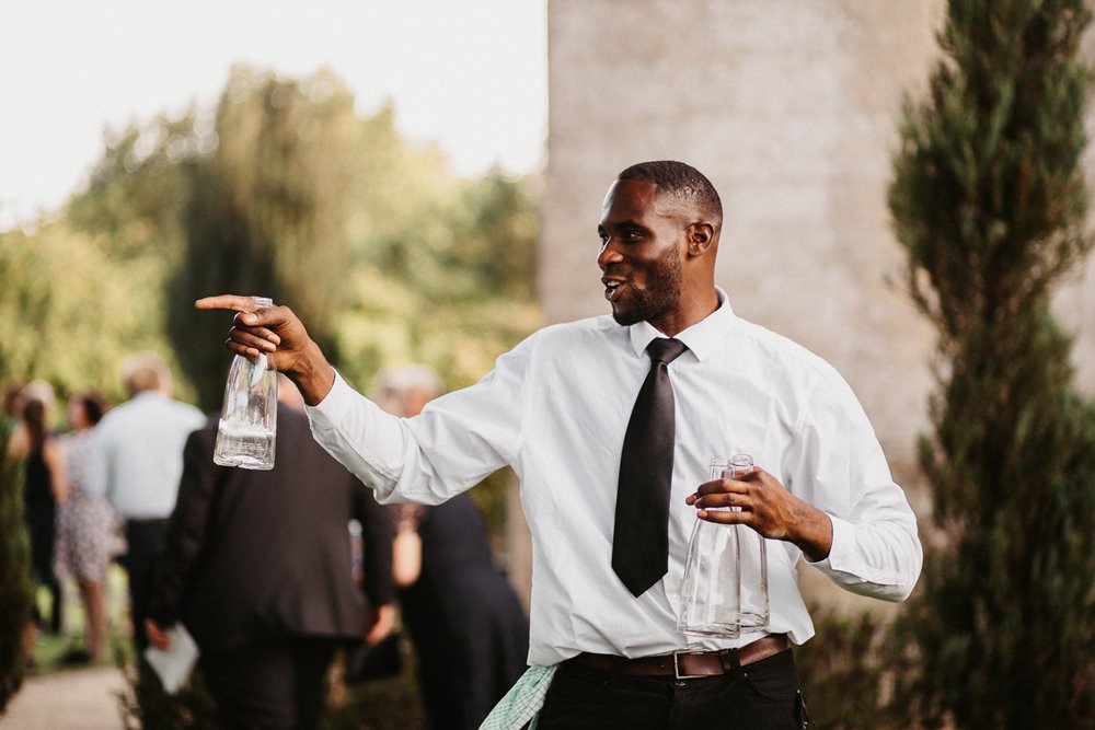 A male wedding guest with bottles in hand dances/ poses candidly