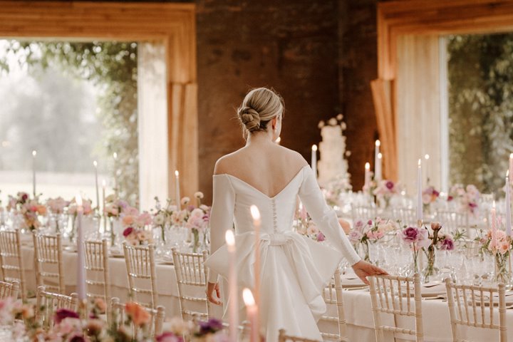Luxe bride surveying her romantic high end wedding reception in March with pink flowers and candles on long white tables