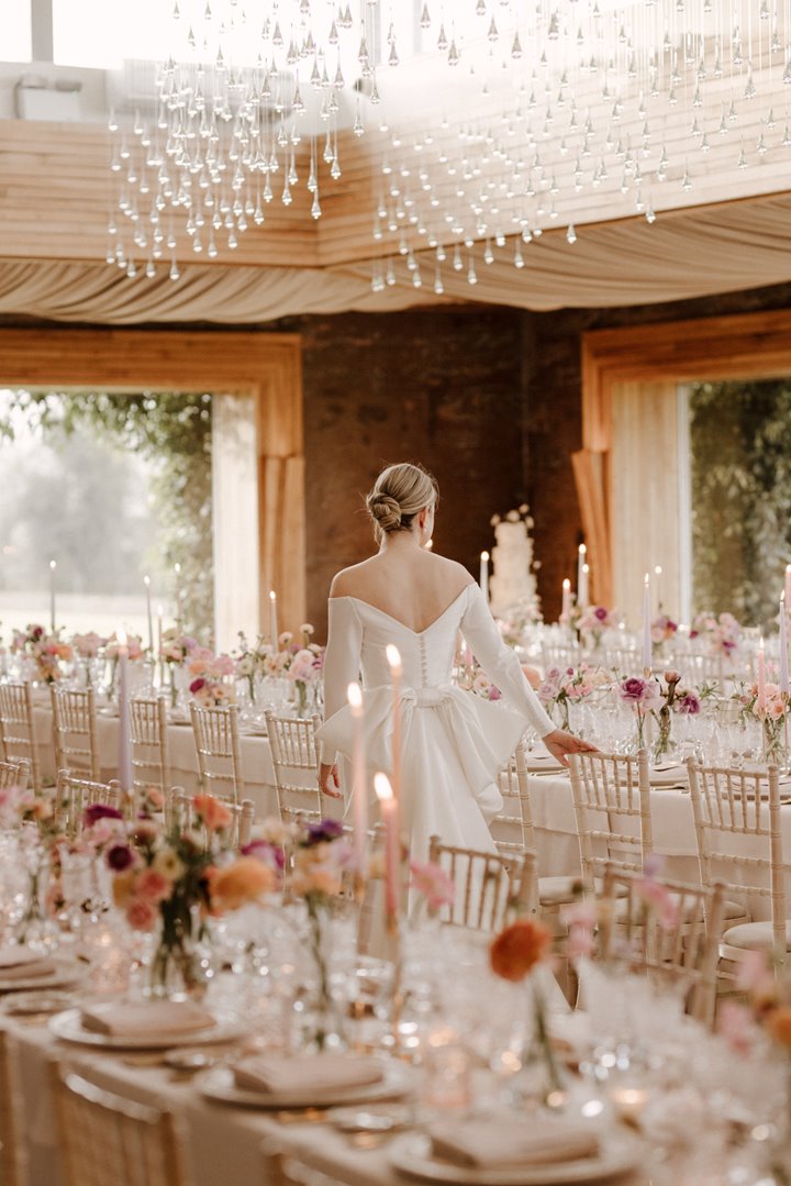Luxe bride surveying her romantic high end wedding reception in March with pink flowers and candles on long white tables
