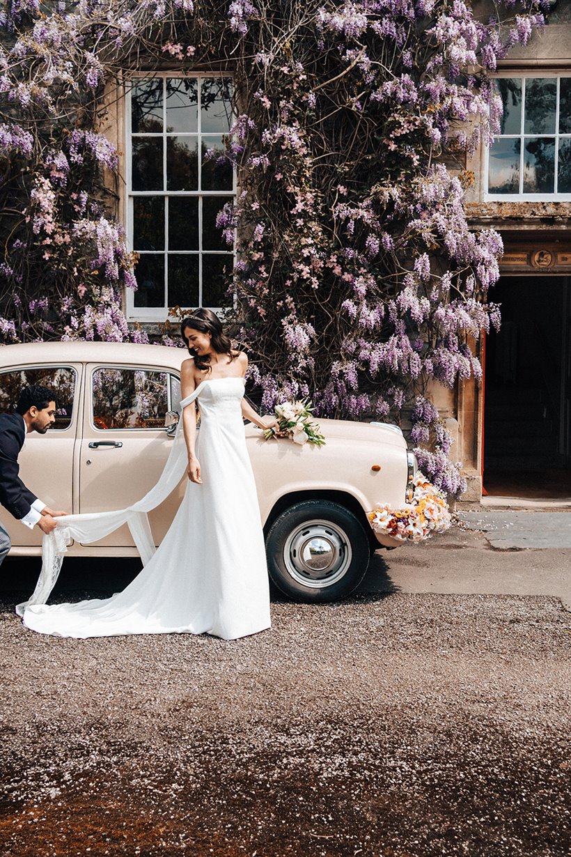 unique wedding car an indian ambassador with flowers decorating the front outside stately home wedding venue elmore court covered in wisteria