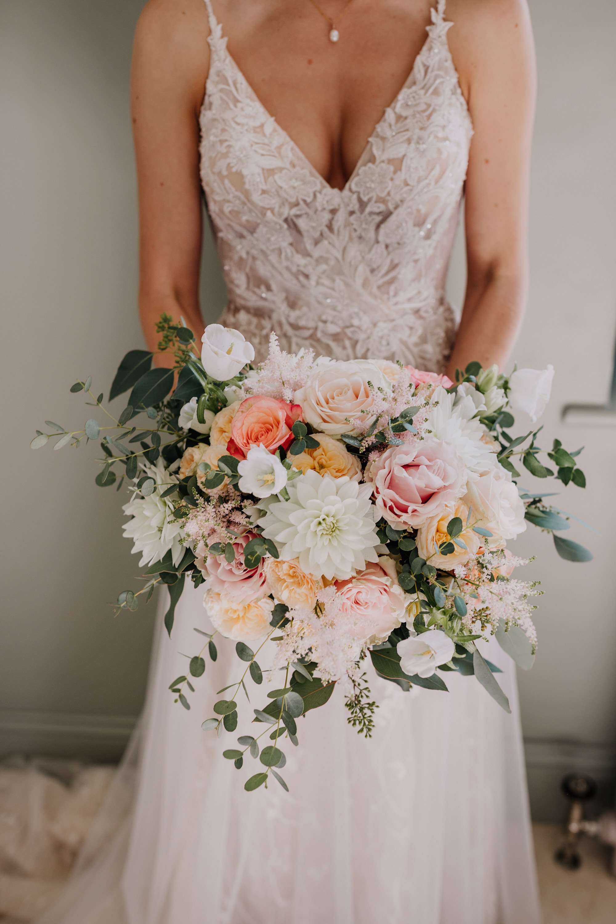 Bride in lace and tulle blush pink wedding dress with pearl necklace and huge bouquet of pink flowers