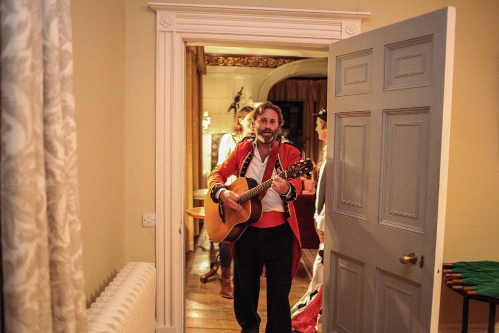 Hamish Guerrini the white rabbit of Glastonbury festival playing guitar in a red coat at a party at mansion house wedding venue elmore court