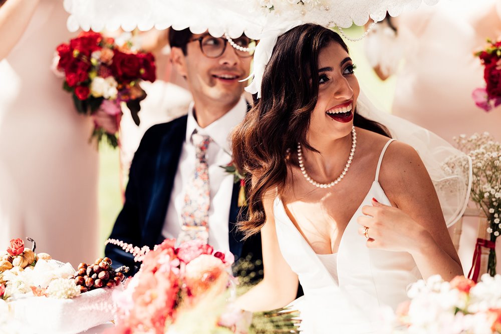 smiling bride and groom underneith silk veil at their persian sugar wedding ceremony at cotswolds wedding venue elmore court