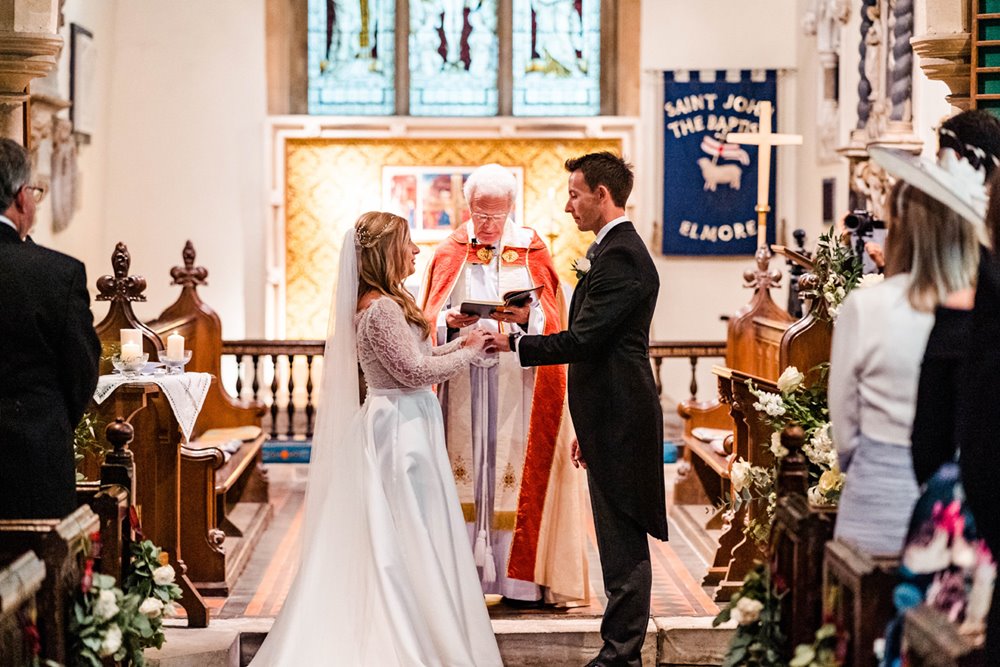 Couple hold hands with vicar behind them at church wedding in elmore england