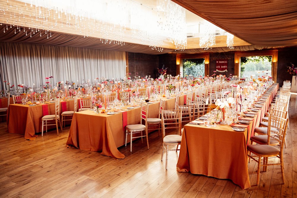 Orange tables with bright flowers for a vibrant wedding reception at eco venue in the cotswolds