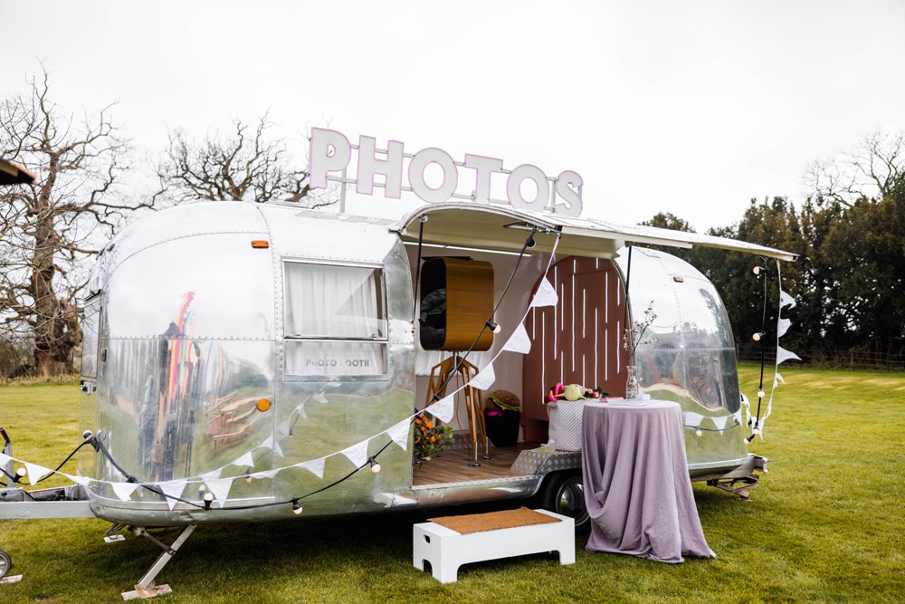 Cool silver trailer caravan photo booth with pink neon lights and bunting at unusual wedding venue elmore court