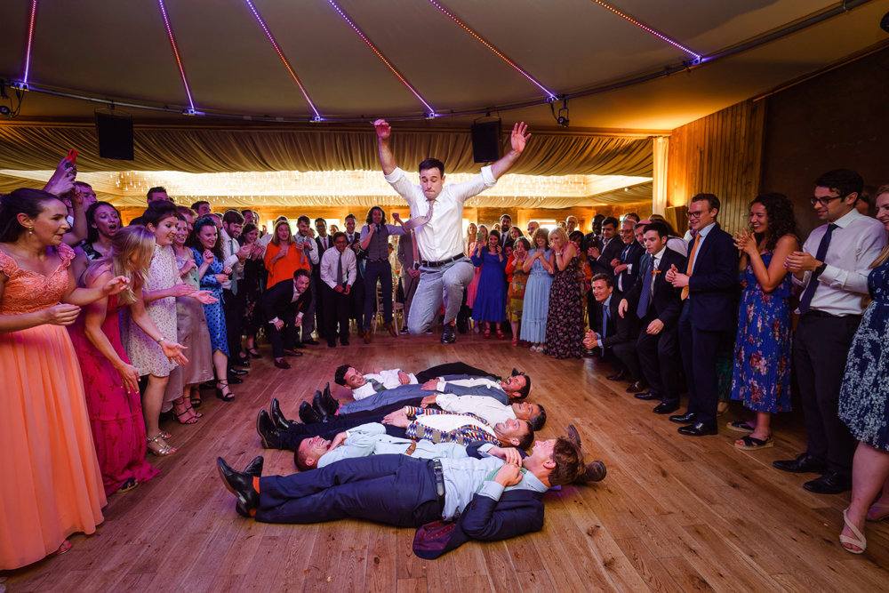 Groom jumps over guests lying on floor at fun party jewish wedding reception