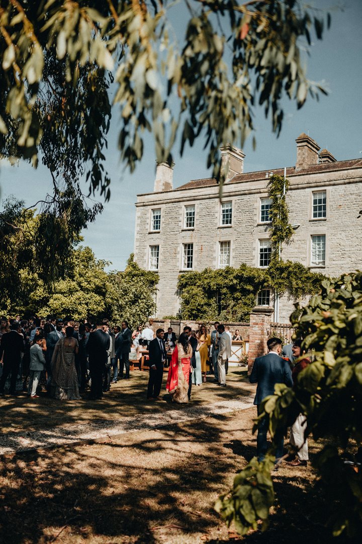 a summer wedding in the walled garden of stately home wedding venue elmore court. Guests relaxed and enjoy the dappled sunshine at drinks reception in the orchard