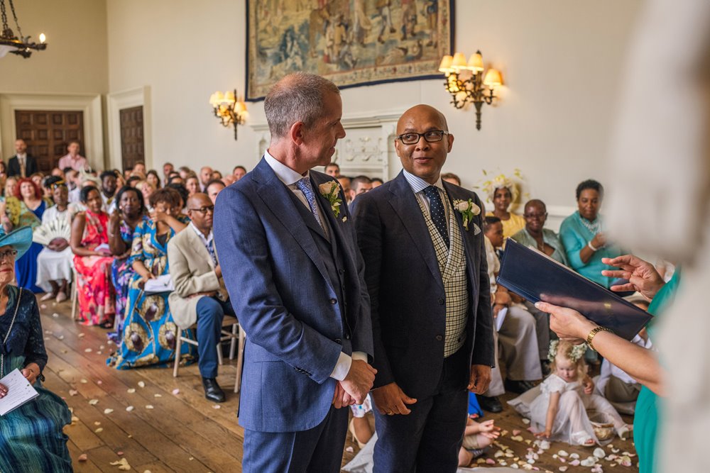 Two grooms look lovingly at each other at the end of the aisle at their gay wedding ceremony in stately home