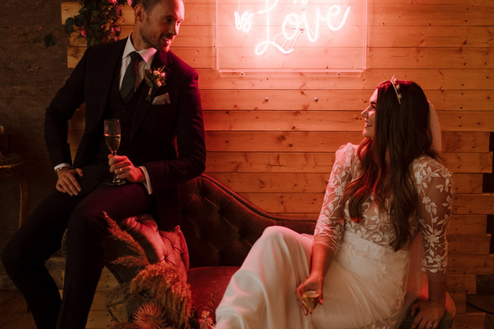 Modern pink boho luxe September wedding couple pose in front of their all you need is love sign at eco wedding venue