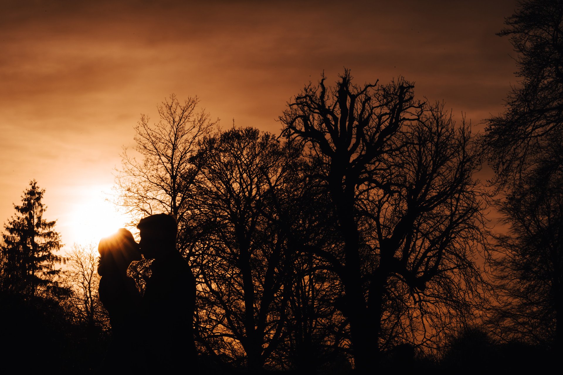 Newlywed couple kiss against an orange sunset sky at Elmore Court