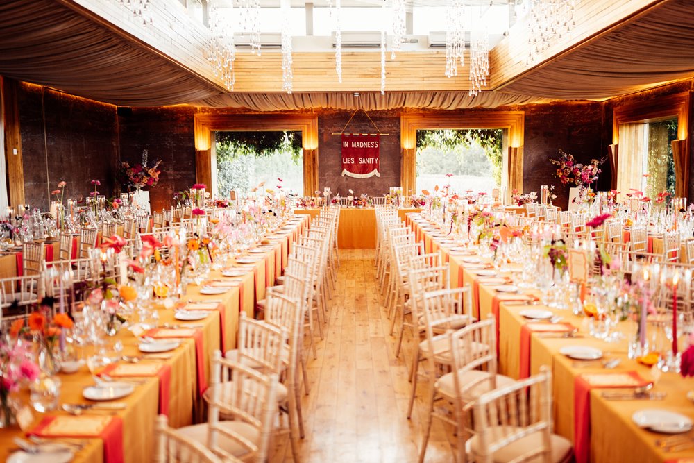 Colourful wedding theme. Orange tables with bright flowers at wedding venue in the cotswolds