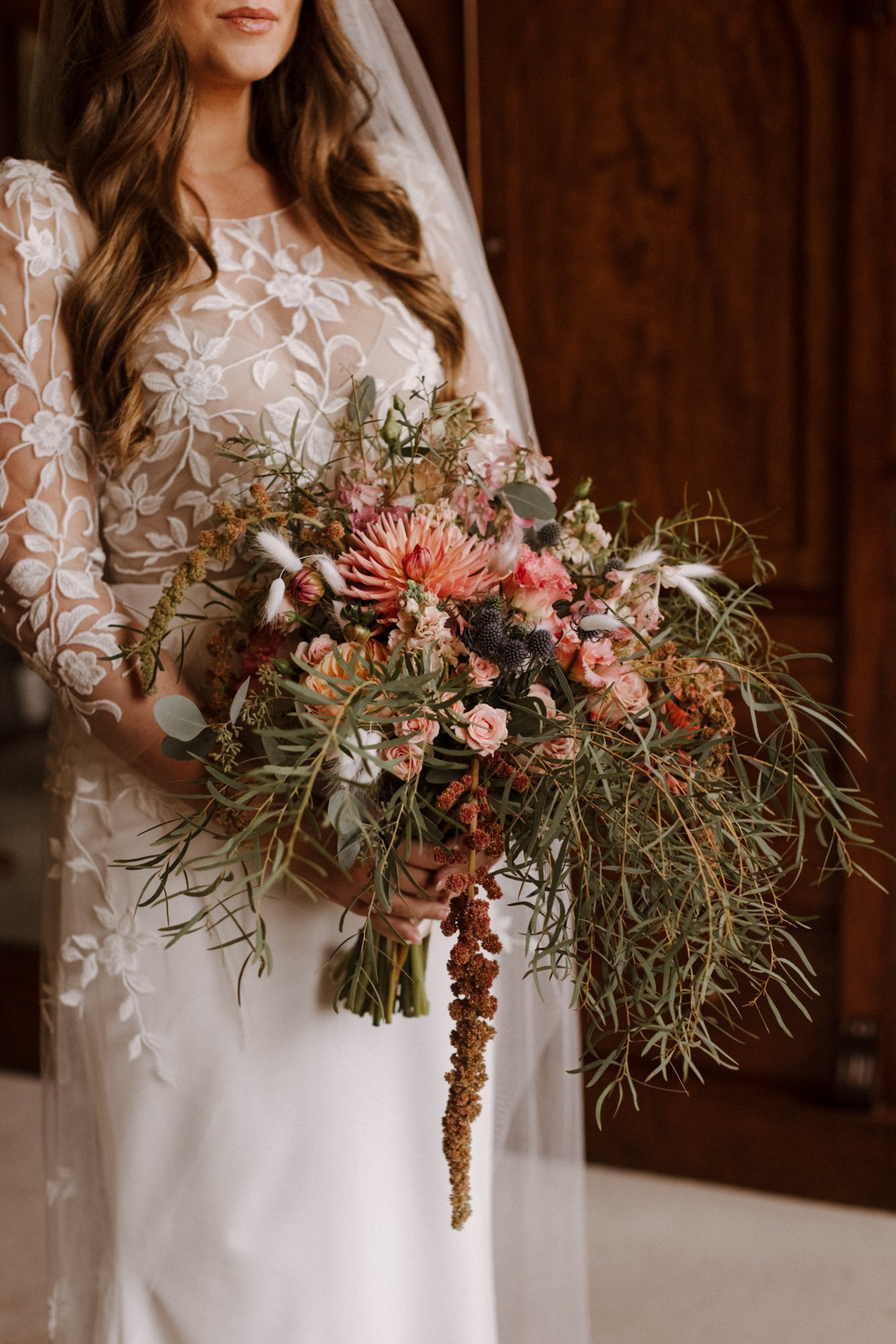 September bride holds big boho bouquet of pink and cream flowers with greenery
