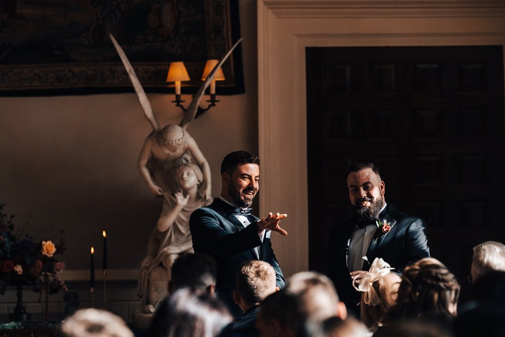 groom in tux in front of angel statues at his wedding ceremony in a historic house in the cotswolds countryside in autumn